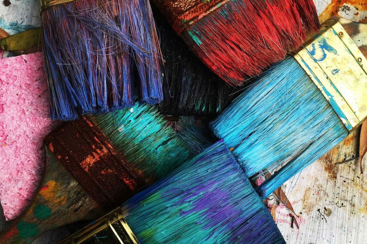 An image of many paintbrushes. They have red, blue, and purple paint on them