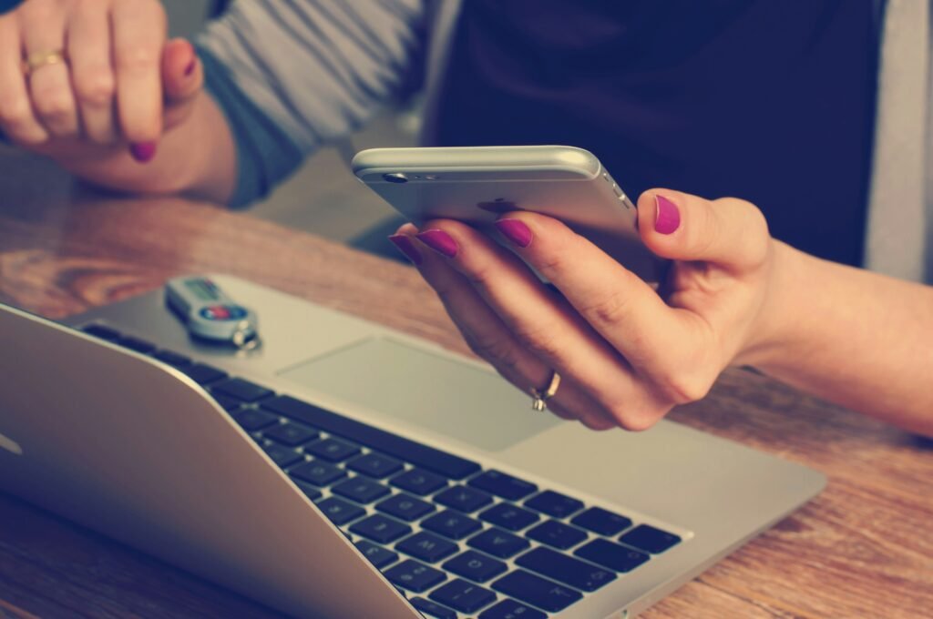 why you absolutely need a new website image: a hand wearing red nail polish holds a phone. a laptop is sitting near them