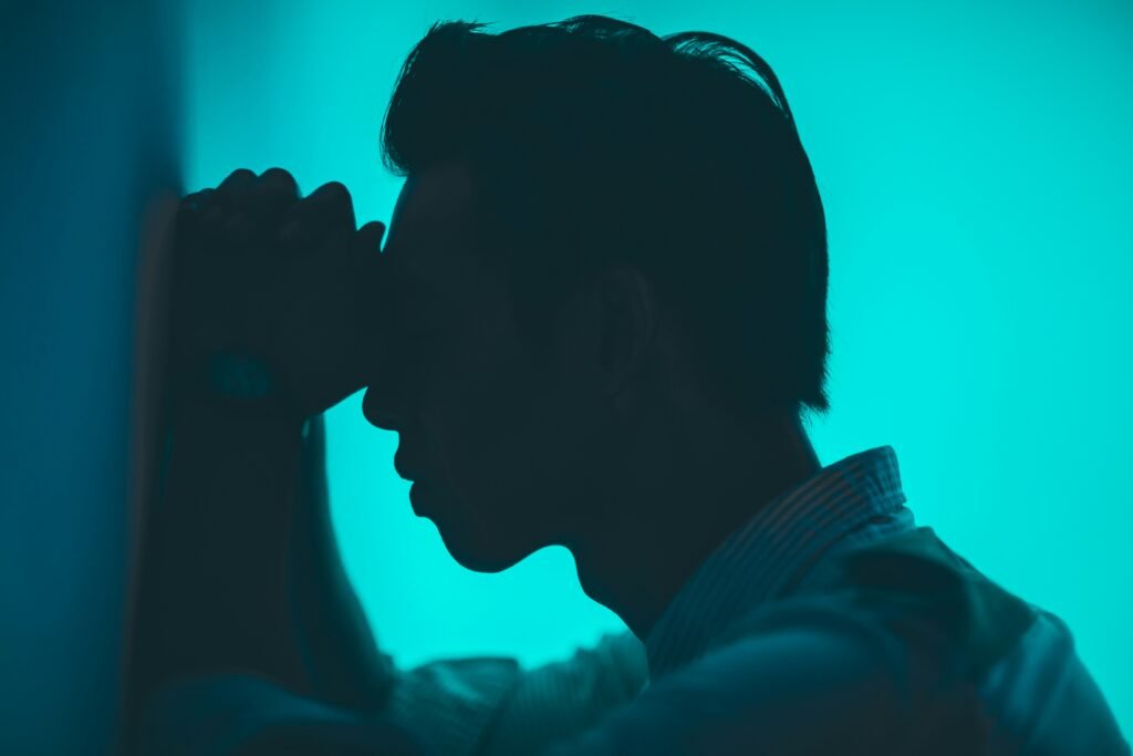 embodied tech work image of a person leaning against a wall. their forehead is resting on their hands, they seem emotionally strained