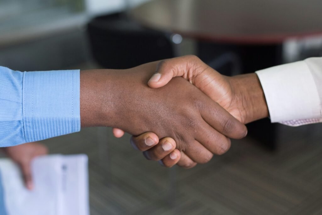 A closeup of two people shaking hands. One is wearing a blue button down shirt, the onther is wearing a white one. This is for an article about SEO